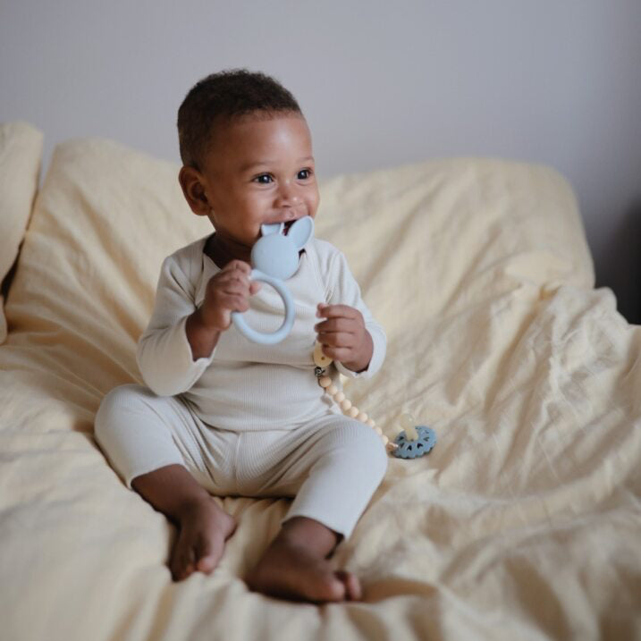 Baby sitting on a bed holding a teething toy