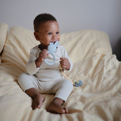 Baby sitting on a bed holding a teething toy